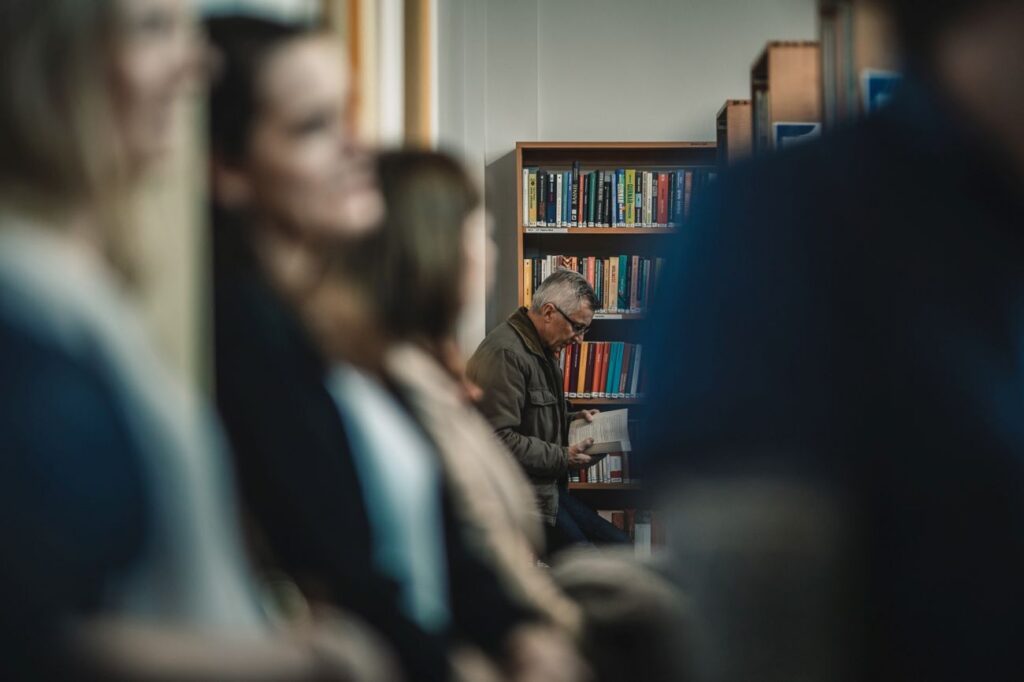 Ludzie słuchają, w dalszym planie pan czyta książkę.